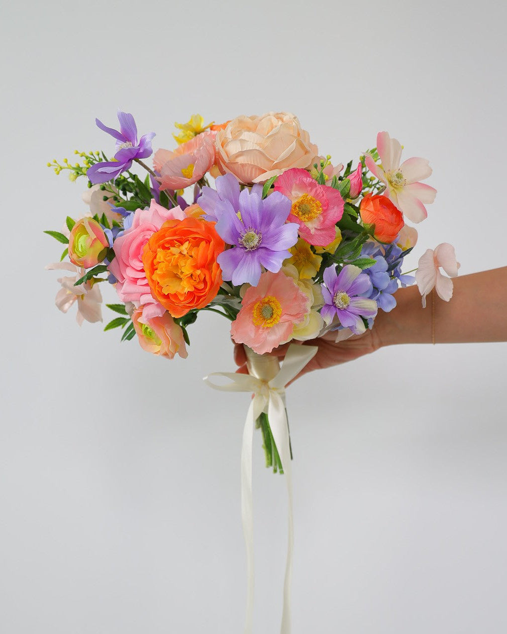 Bouquet of colorful flowers held by a hand against a light gray background