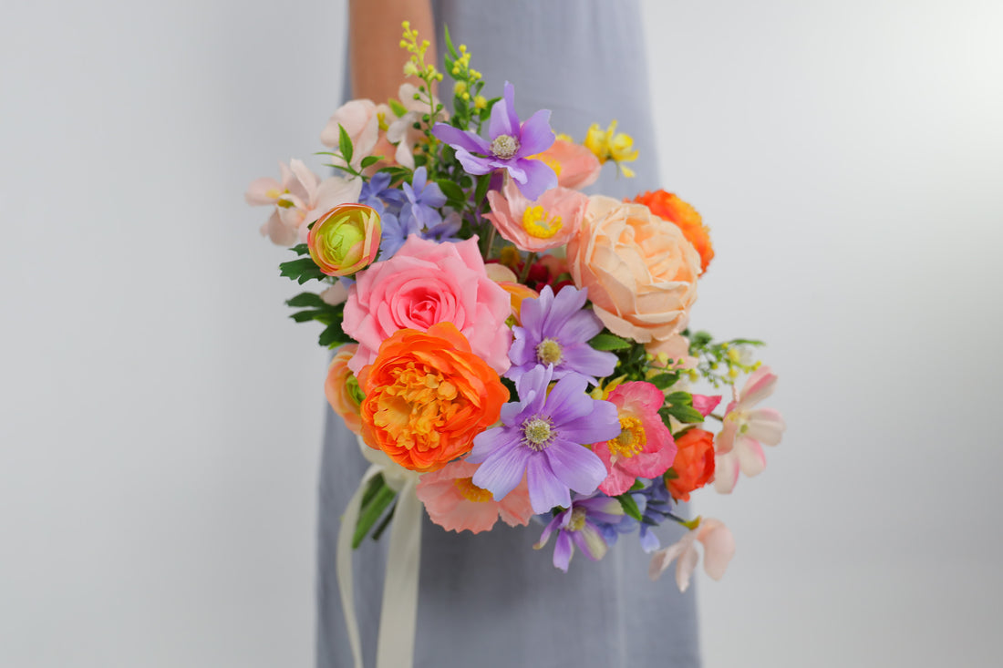 Bouquet of colorful flowers held by a hand against a light gray background