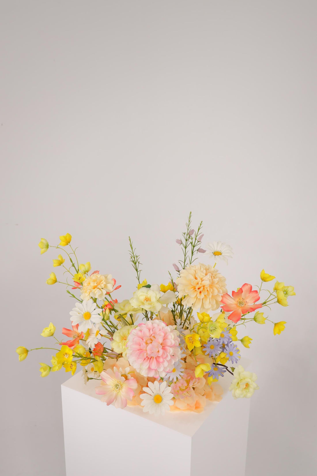 Pastel wildflower silk arrangement in yellow, pink, coral, and blue on a wooden stool